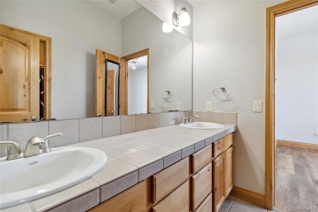 bathroom featuring a sink, backsplash, baseboards, and double vanity