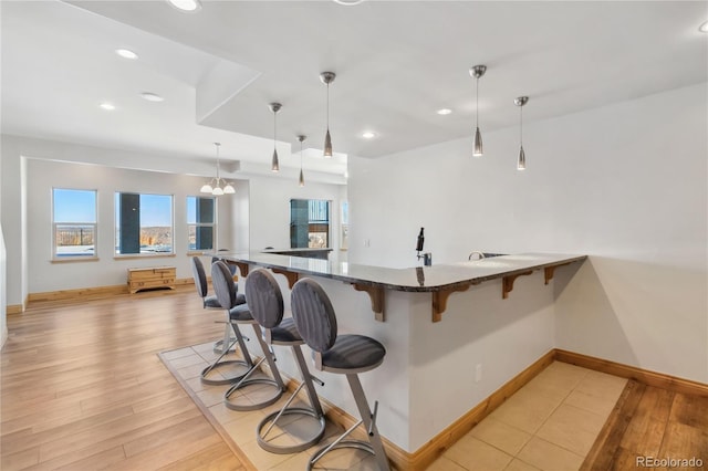 kitchen with light wood-style floors, dark stone counters, a breakfast bar, and decorative light fixtures