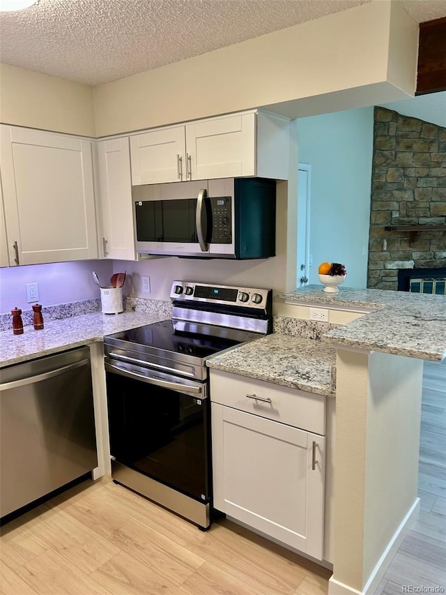 10251 W 44th Ave Unit 3-204, Wheat Ridge, CO 80033 - kitchen with stainless steel appliances, light wood-type flooring, white cabinets, a peninsula, and light stone counters