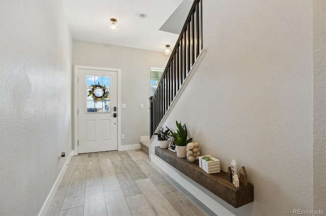 foyer entrance with baseboards, stairs, and light wood-style floors