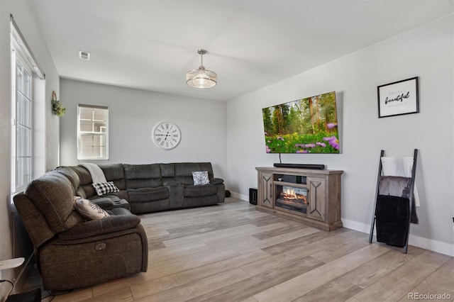 living room featuring a glass covered fireplace, baseboards, and light wood-type flooring