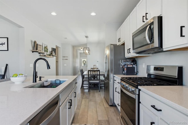 kitchen with a sink, stainless steel appliances, white cabinets, and light wood finished floors