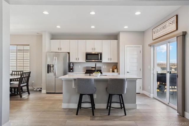 kitchen with light wood finished floors, white cabinets, stainless steel appliances, and an island with sink