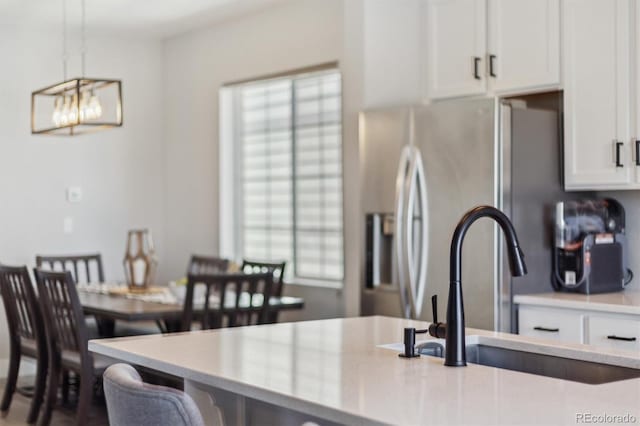 kitchen with decorative light fixtures, light countertops, stainless steel refrigerator with ice dispenser, white cabinets, and a sink