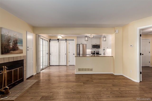 unfurnished living room with a barn door, ceiling fan, dark hardwood / wood-style flooring, and a tile fireplace