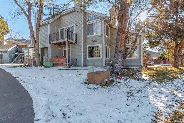 snow covered back of property with central AC and a balcony