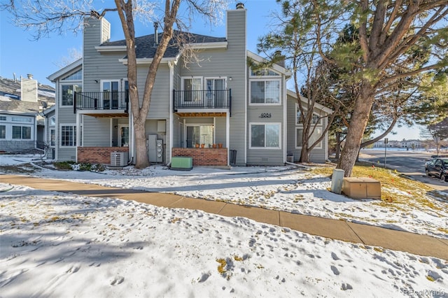 snow covered house featuring cooling unit and a balcony