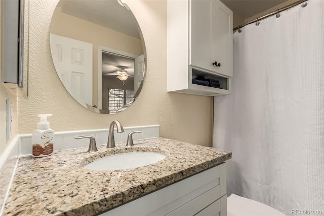 full bath featuring toilet, a textured wall, vanity, and a ceiling fan