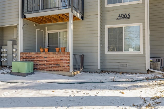 snow covered property entrance featuring crawl space, central AC, and a balcony