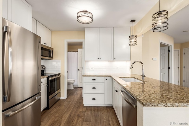 kitchen featuring stainless steel appliances, dark wood-type flooring, a peninsula, a sink, and white cabinetry