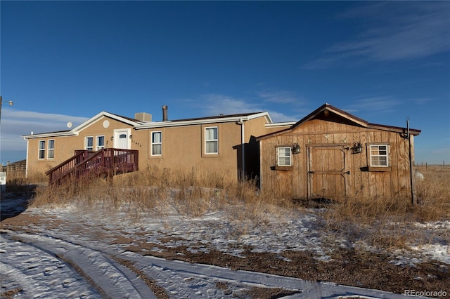 snow covered back of property with a shed and a wooden deck