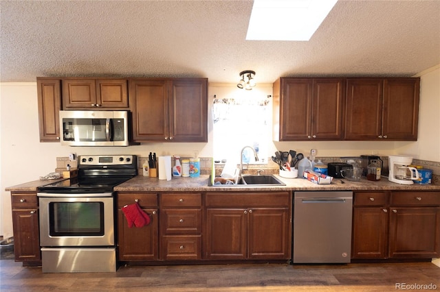 kitchen with appliances with stainless steel finishes, a textured ceiling, sink, and dark wood-type flooring