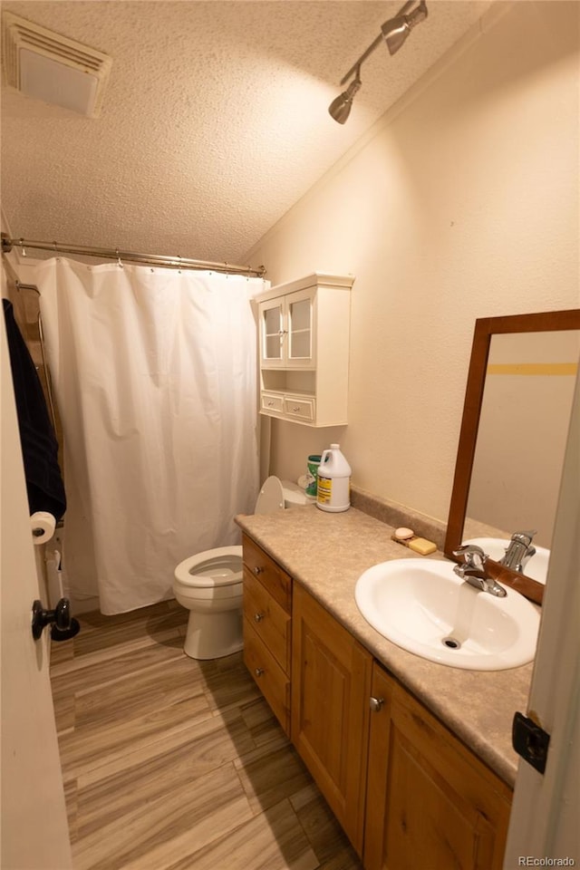 bathroom featuring wood-type flooring, a textured ceiling, lofted ceiling, vanity, and toilet