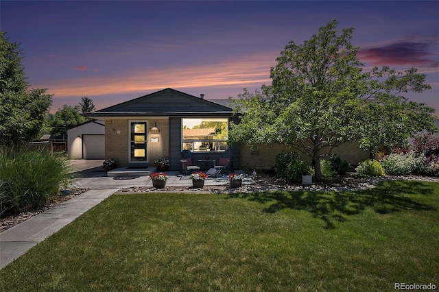 6868 S Birch Way, Centennial, CO 80122 - back of property at dusk featuring a lawn, concrete driveway, brick siding, and an outdoor structure