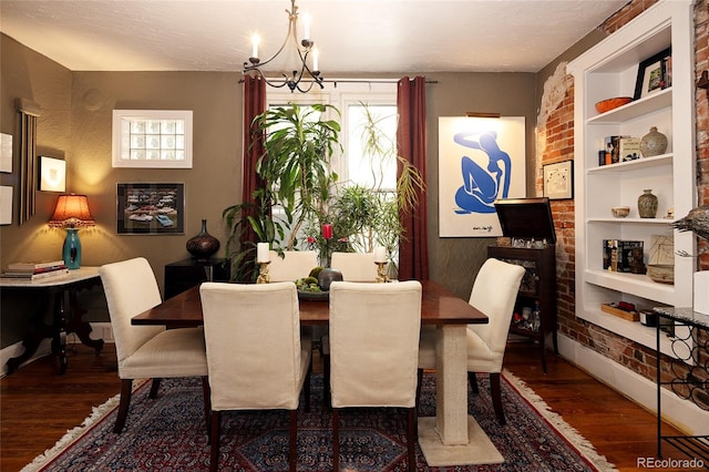 dining room with built in shelves, dark wood-type flooring, brick wall, and a notable chandelier