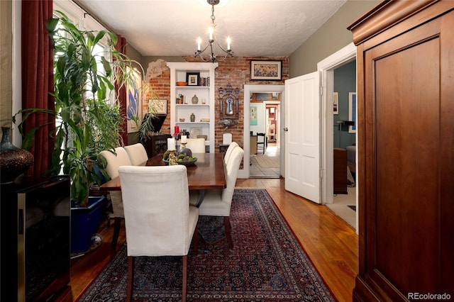 dining space with wood-type flooring, a textured ceiling, a notable chandelier, and brick wall