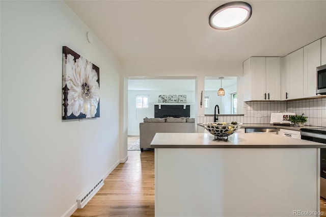5563 Newland Way, Arvada, CO 80002 - kitchen with a baseboard radiator, backsplash, light wood-style flooring, a fireplace, and white cabinets