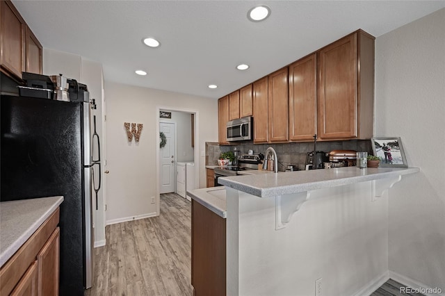 kitchen with stainless steel appliances, tasteful backsplash, kitchen peninsula, a breakfast bar area, and light wood-type flooring