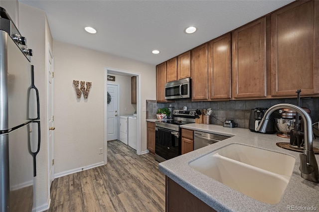 kitchen with decorative backsplash, stainless steel appliances, washer and clothes dryer, sink, and light hardwood / wood-style floors