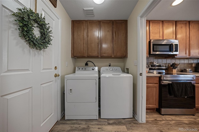 laundry area with washing machine and dryer, light hardwood / wood-style flooring, cabinets, and a textured ceiling