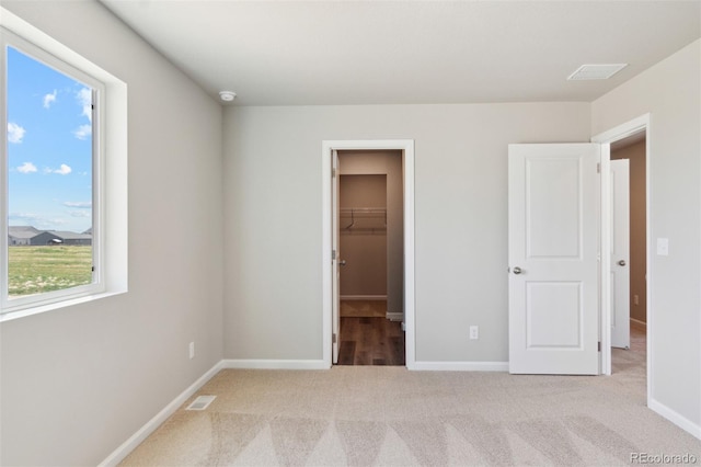 unfurnished bedroom featuring light carpet, baseboards, and a walk in closet