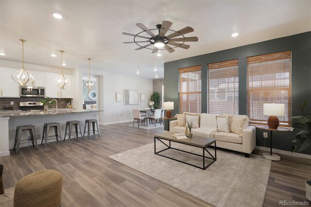 living room with hardwood / wood-style floors, ceiling fan with notable chandelier, and sink