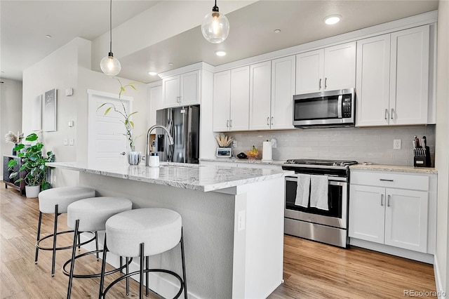 1575 W 68th Ave, Denver, CO 80221 - kitchen featuring stainless steel appliances, tasteful backsplash, light wood finished floors, a kitchen breakfast bar, and white cabinets