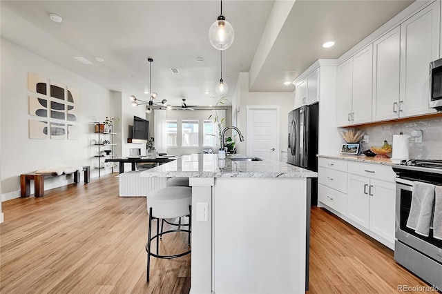 1575 W 68th Ave, Denver, CO 80221 - kitchen featuring stainless steel appliances, an island with sink, decorative backsplash, white cabinetry, and a kitchen bar