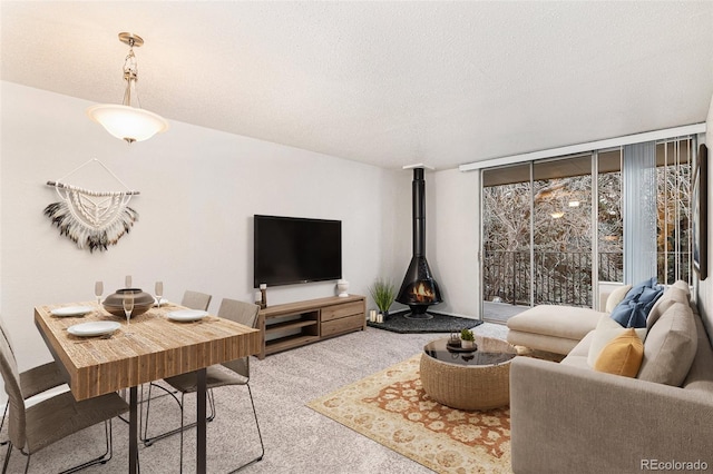 living room featuring a wood stove, light colored carpet, a textured ceiling, and a wall of windows