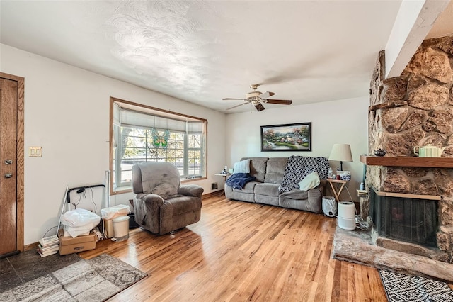 living room featuring ceiling fan, light wood-type flooring, and a fireplace