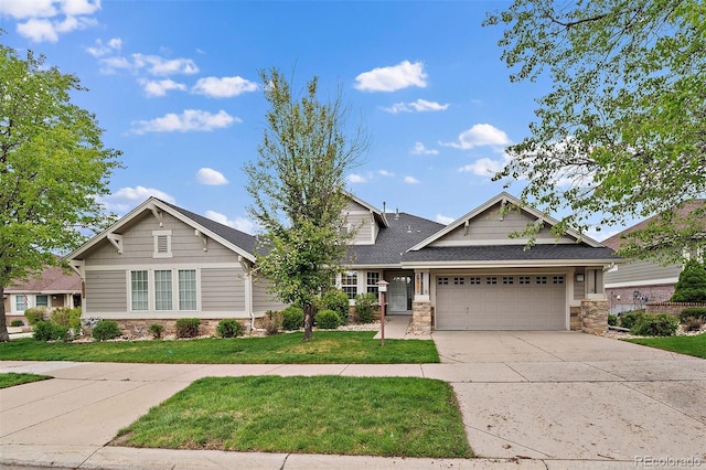 craftsman-style house featuring stone siding, an attached garage, driveway, a front yard, and roof with shingles