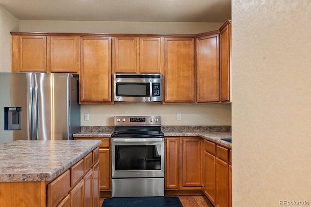 kitchen with appliances with stainless steel finishes, brown cabinets, and wood finished floors