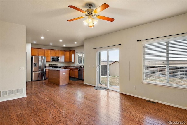 kitchen with dark wood-style flooring, brown cabinets, stainless steel appliances, visible vents, and a kitchen island