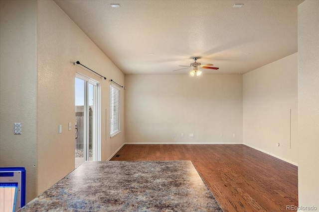 unfurnished room with ceiling fan, a textured ceiling, baseboards, and wood finished floors