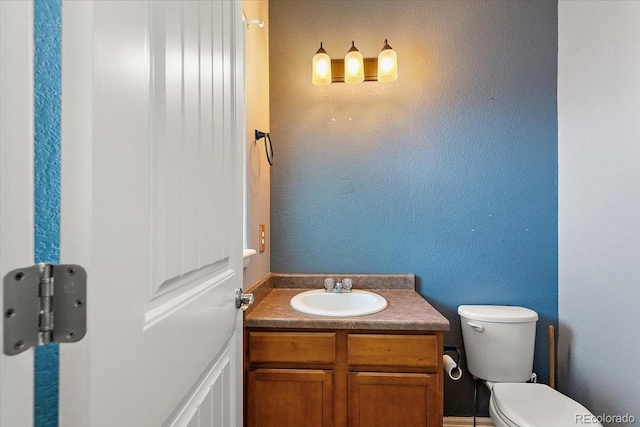 half bath with a textured wall, vanity, and toilet