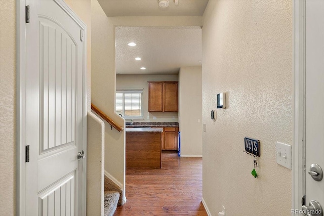 corridor featuring recessed lighting, a textured wall, dark wood-type flooring, baseboards, and stairs