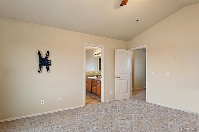 unfurnished bedroom featuring lofted ceiling, light colored carpet, connected bathroom, and baseboards