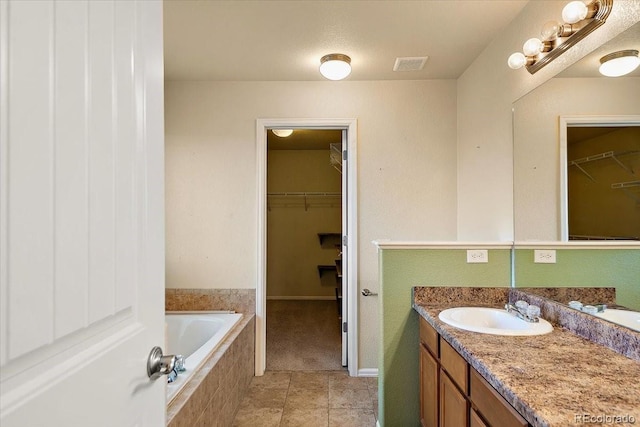 bathroom with a relaxing tiled tub, visible vents, tile patterned floors, a walk in closet, and vanity