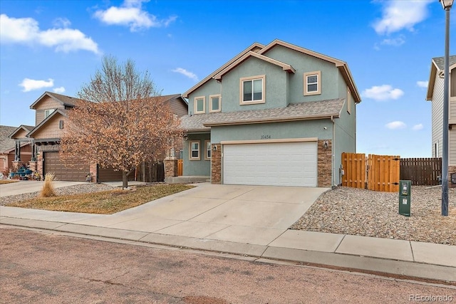 traditional-style house with a shingled roof, fence, driveway, stone siding, and stucco siding