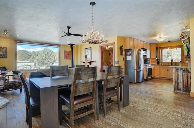 dining space featuring sink, an inviting chandelier, wood-type flooring, a textured ceiling, and a wood stove