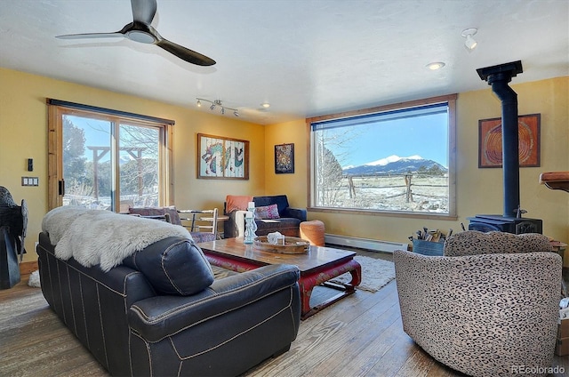 living room featuring a healthy amount of sunlight, a mountain view, a wood stove, and baseboard heating