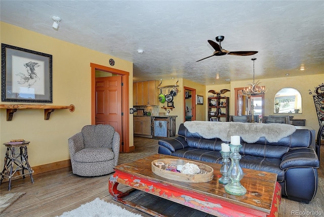 living room with ceiling fan with notable chandelier, light hardwood / wood-style floors, and a textured ceiling