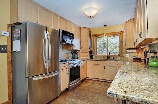 kitchen with light brown cabinetry, decorative light fixtures, sink, stainless steel appliances, and light stone countertops