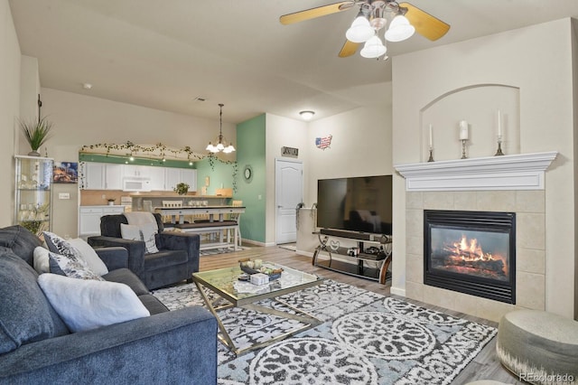 living area featuring baseboards, ceiling fan with notable chandelier, wood finished floors, and a tile fireplace