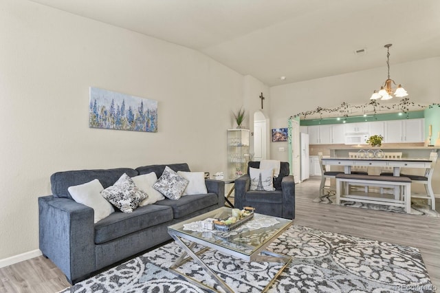 living room with visible vents, arched walkways, baseboards, light wood finished floors, and a chandelier