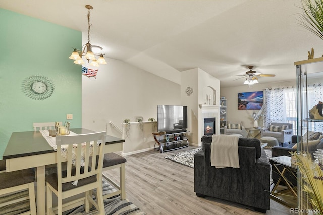 living room with a fireplace, vaulted ceiling, wood finished floors, baseboards, and ceiling fan with notable chandelier