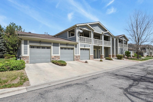 craftsman-style house with a balcony, concrete driveway, and stone siding