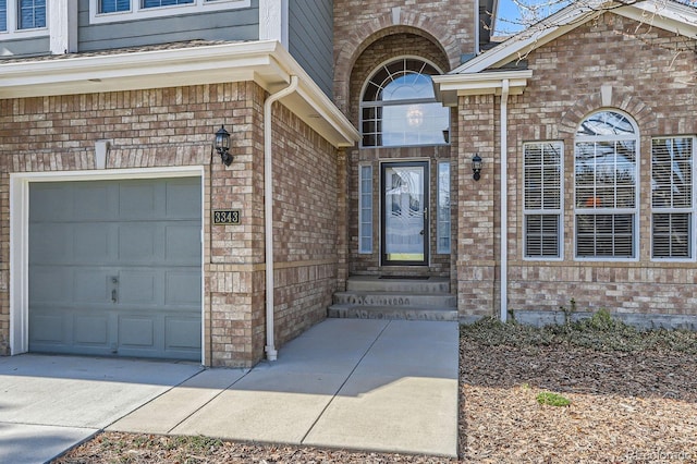 entrance to property with an attached garage, concrete driveway, and brick siding