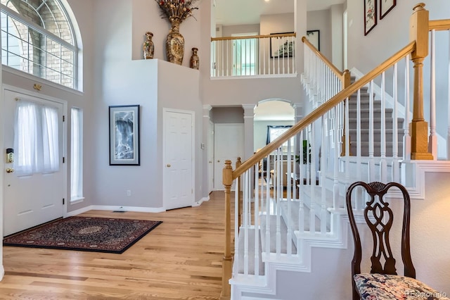 foyer featuring baseboards, ornate columns, a high ceiling, and wood finished floors