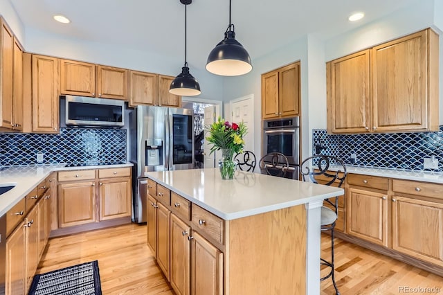 kitchen featuring light wood finished floors, appliances with stainless steel finishes, decorative backsplash, and a kitchen breakfast bar